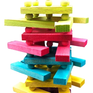 May include: A colorful wooden bird toy with multiple layers of different colored wood and beads. The toy is suspended from a metal hook.