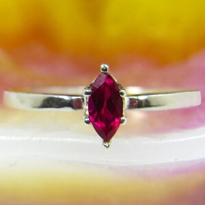 Könnte beinhalten: Ein silberner Ring mit einem rubinroten Marquise-Schliff.