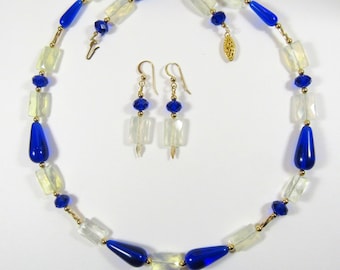 Peut inclure: Un collier et des boucles d'oreilles assortis composés de perles de verre bleues et blanches. Le collier a une forme de goutte et les boucles d'oreilles sont rectangulaires.