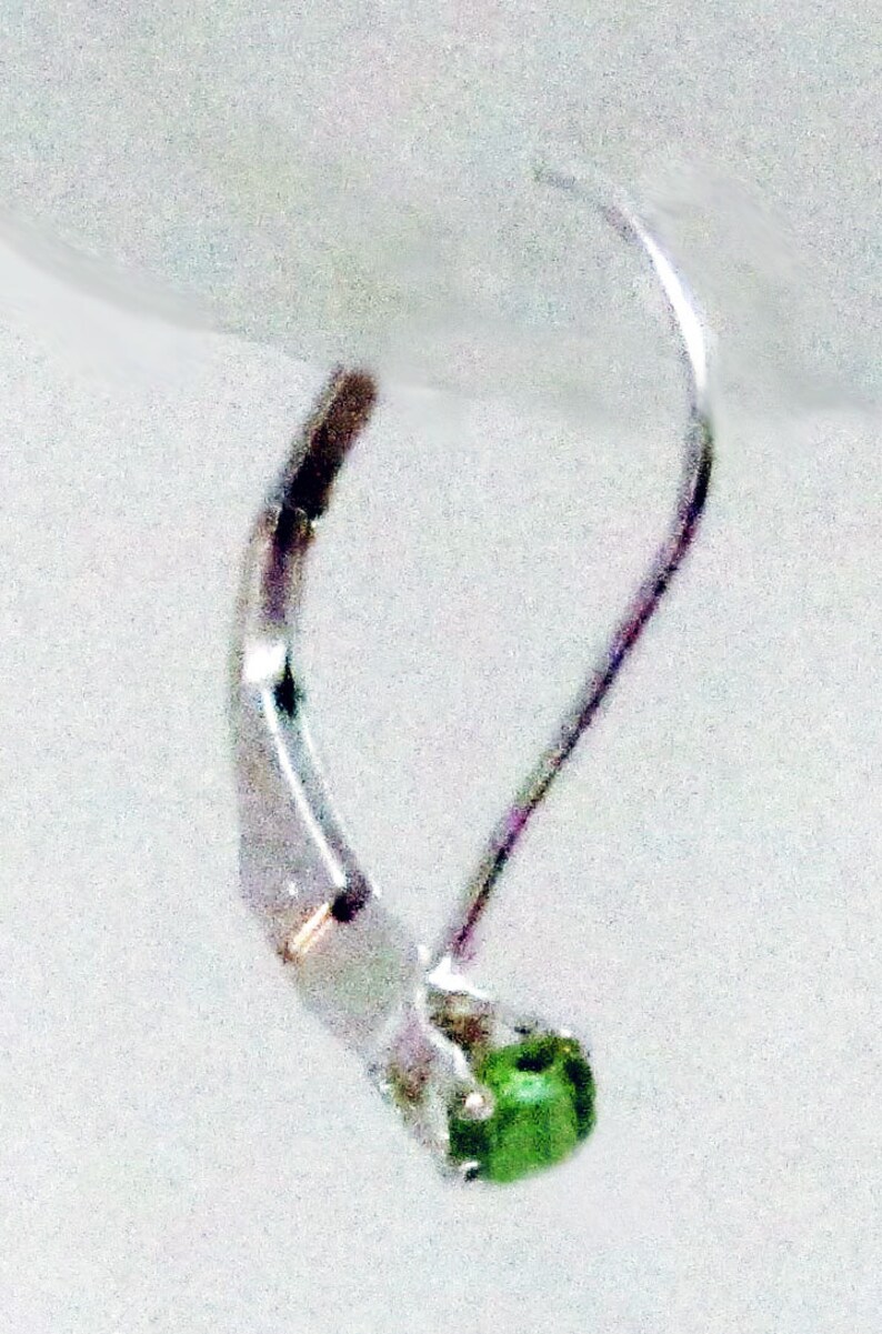 May include: Silver earring with a green gemstone. The earring has a simple, elegant design.