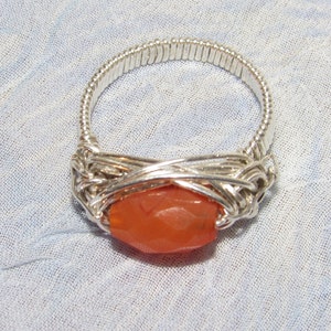 May include: A silver wire wrapped ring with a large, orange carnelian stone.