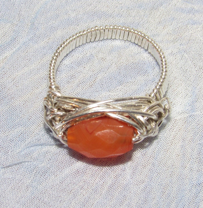 May include: A silver wire wrapped ring with a large, orange carnelian stone.
