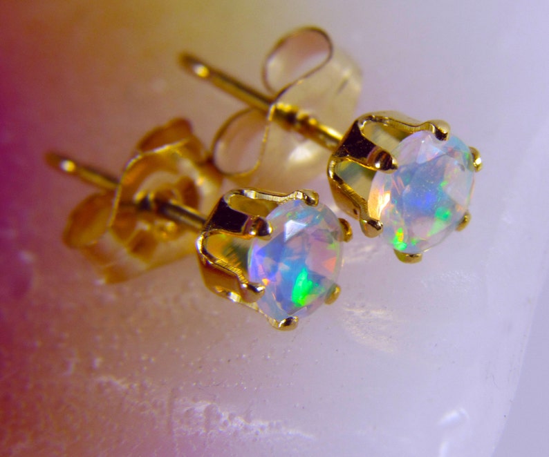 May include: A pair of gold stud earrings with iridescent opal gemstones. The earrings have a simple, classic design.