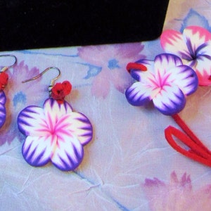 Peut inclure: Un ensemble de boucles d'oreilles et d'un collier assorti en forme de fleurs violettes et blanches. Les fleurs sont en p&acirc;te polym&egrave;re et ont un centre rose. Le collier est fait d'un cordon rouge.
