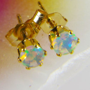 May include: A pair of gold stud earrings with iridescent opal gemstones. The earrings have a classic design and are perfect for everyday wear.