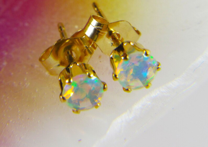 May include: A pair of gold stud earrings with iridescent opal gemstones. The earrings have a classic design and are perfect for everyday wear.