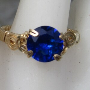 Puede incluir: Un anillo de alambre dorado con una gran piedra preciosa redonda azul.