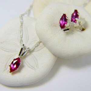 Puede incluir: Un conjunto de pendientes y un colgante de plata de ley con una piedra preciosa rosa en forma de marquesa.