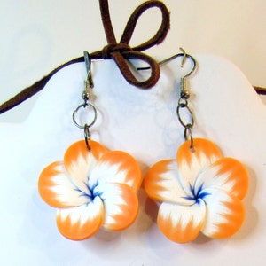 Peut inclure: Une paire de boucles d'oreilles en forme de fleurs orange et blanches avec des centres bleus. Les boucles d'oreilles sont en p&acirc;te polym&egrave;re et ont des crochets argent&eacute;s.
