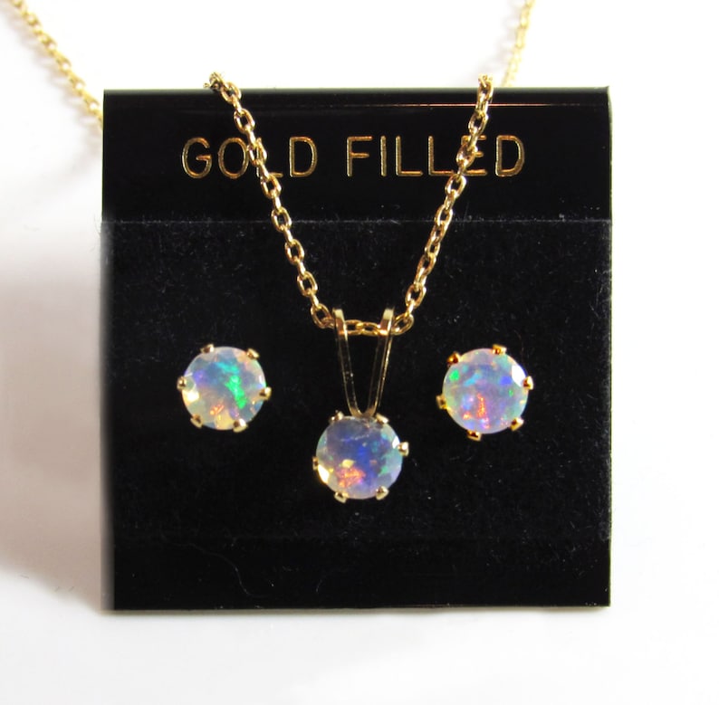 May include: A gold filled necklace and earrings set with opal stones. The necklace has a simple chain and a round pendant with an opal stone. The earrings are stud earrings with round opal stones.