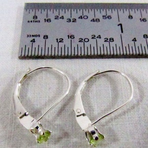 May include: A pair of silver leverback earrings with green gemstones. The earrings are measured against a ruler.