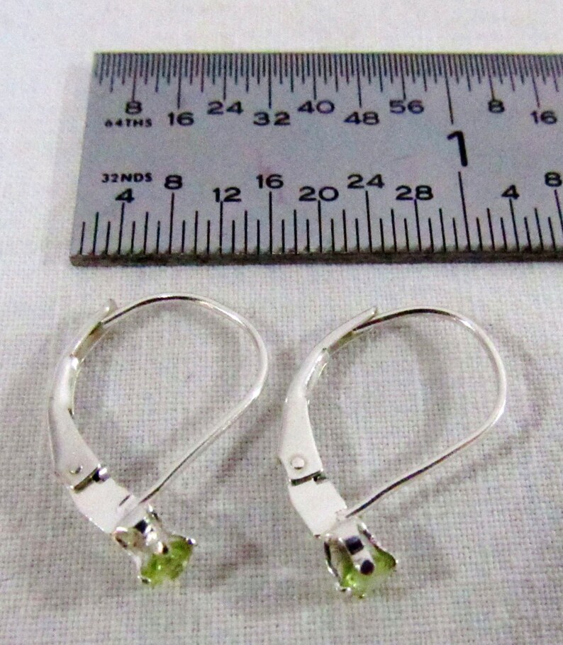 May include: A pair of silver leverback earrings with green gemstones. The earrings are measured against a ruler.