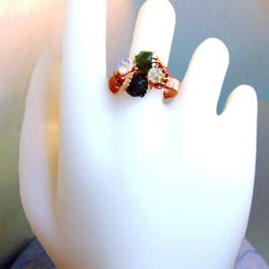 Puede incluir: Un anillo de alambre de cobre con piedras verdes y transparentes. El anillo est&aacute; envuelto en alambre de cobre y tiene un grupo de piedras en el centro.