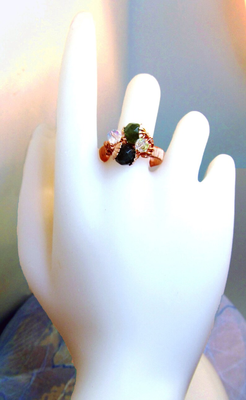 Puede incluir: Un anillo de alambre de cobre con piedras verdes y transparentes. El anillo est&aacute; envuelto en alambre de cobre y tiene un grupo de piedras en el centro.