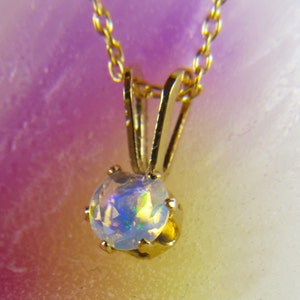 May include: A gold chain necklace with a round opal pendant. The opal is iridescent with flashes of blue, green, and yellow.