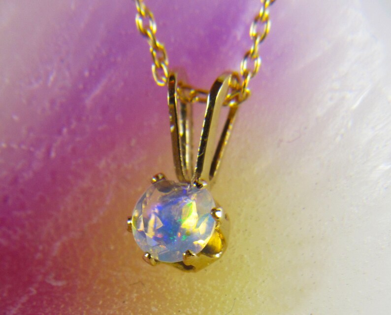 May include: A gold chain necklace with a round opal pendant. The opal is iridescent with flashes of blue, green, and yellow.