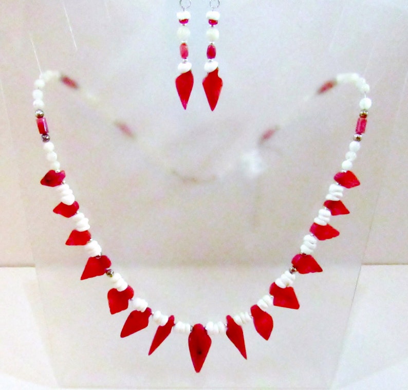 K&ouml;nnte beinhalten: Ein rotes und wei&szlig;es Halsketten- und Ohrring-Set mit tropfenf&ouml;rmigen Perlen. Die Halskette hat eine silberne Kette und die Ohrringe haben silberne Haken.