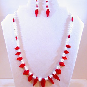 K&ouml;nnte beinhalten: Eine rote und wei&szlig;e Perlenkette mit spitzem Design und passenden Ohrringen. Die Kette und die Ohrringe bestehen aus roten und wei&szlig;en Perlen.