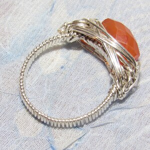 May include: A silver wire wrapped ring with a large, faceted, orange carnelian gemstone.