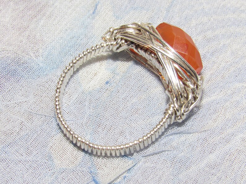 May include: A silver wire wrapped ring with a large, faceted, orange carnelian gemstone.