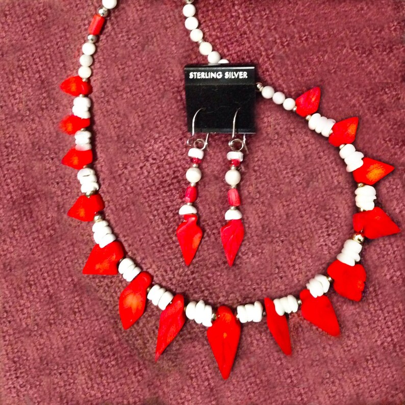 K&ouml;nnte beinhalten: Eine rot-wei&szlig;e Perlenkette und passende Ohrringe mit einem Sterling-Silber-Anh&auml;nger. Die Kette besteht aus roten tropfenf&ouml;rmigen Perlen und wei&szlig;en runden Perlen.