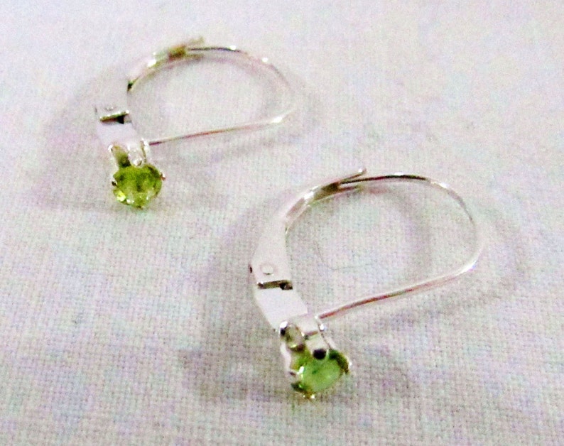 May include: A pair of silver earrings with green gemstone accents. The earrings have a lever back closure.