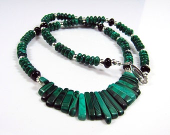 May include: A green malachite necklace with a pendant made of multiple malachite stones. The necklace is made with silver and black beads.