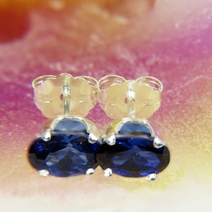 Puede incluir: Un par de pendientes de plata con piedras ovaladas de color azul oscuro.