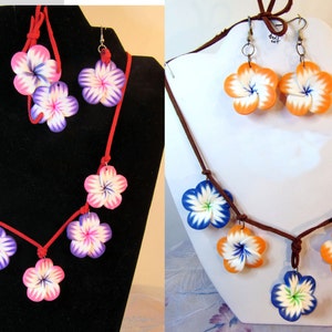 Peut inclure: Deux ensembles de bijoux en forme de fleurs, l'un avec des fleurs roses, blanches et violettes et l'autre avec des fleurs orange, blanches et bleues. Les deux ensembles comprennent un collier et des boucles d'oreilles.