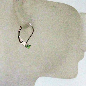 May include: A silver hoop earring with a small green gemstone in the shape of a heart.
