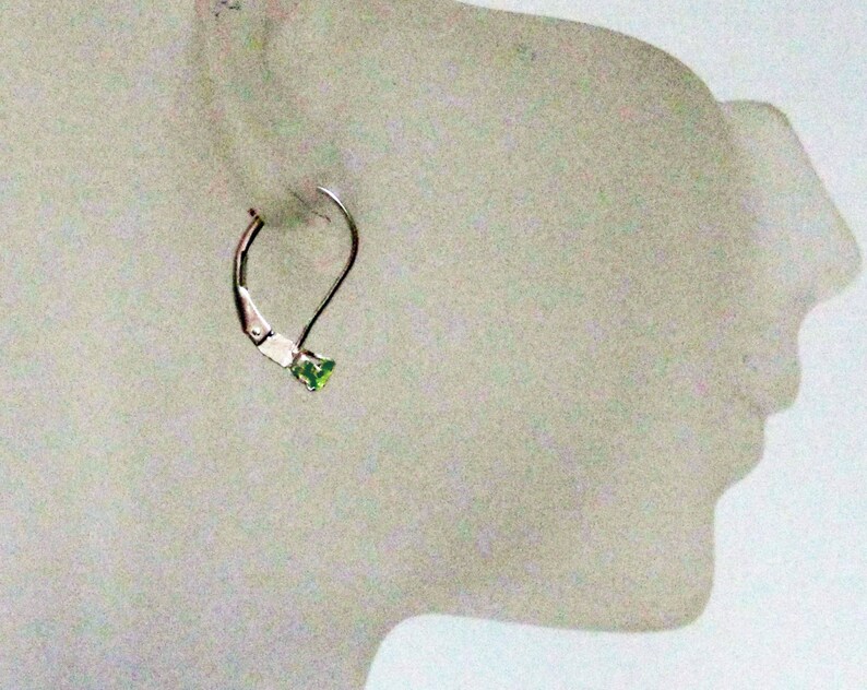 May include: A silver hoop earring with a small green gemstone in the shape of a heart.