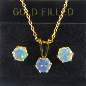 May include: A gold filled necklace and earrings set with a white opal pendant and matching earrings. The jewelry is displayed in a black box with the words "GOLD FILLED" printed on the top.
