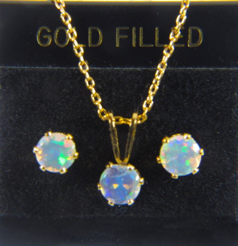 May include: A gold filled necklace and earrings set with a white opal pendant and matching earrings. The jewelry is displayed in a black box with the words "GOLD FILLED" printed on the top.