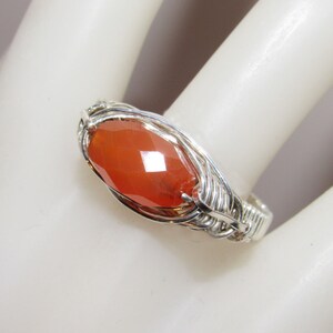 May include: A silver wire wrapped ring with a large, faceted carnelian gemstone. The carnelian is a deep orange color.
