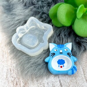 May include: A blue silicone mould of a cartoon cat with a rain cloud inside. The mould is next to a blue cat figurine with a rain cloud inside.