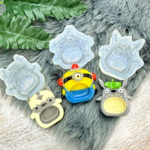 May include: Five silicone molds for making resin crafts. The molds are shaped like a Totoro, a Minion, a Yeti, a cat, and a house. The molds are clear and have a smooth surface.