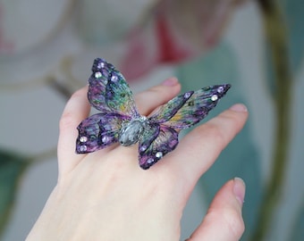 May include: A ring featuring a purple and green butterfly with iridescent wings and rhinestones.