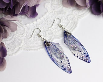 May include: A pair of silver earrings with blue and white iridescent wings and silver flower accents. The wings have a delicate, translucent quality.