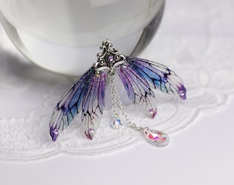 May include: A pair of iridescent purple and blue fairy wings with a silver chain and crystal accents.