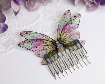 May include: A silver hair comb with a pink, green, and iridescent butterfly design. The butterfly has glitter accents and a clear rhinestone in the centre.