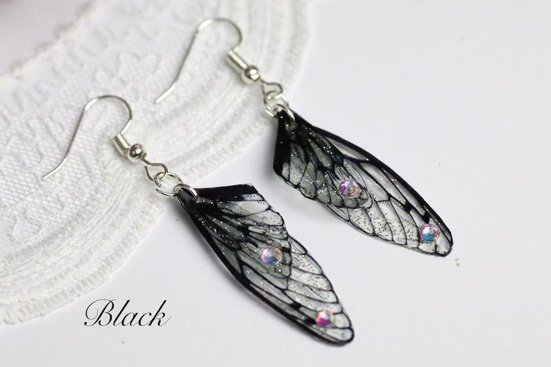 May include: Black insect wing earrings with iridescent rhinestones. The wings are translucent with black veins and glitter.