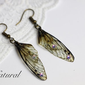 May include: A pair of earrings featuring delicate, translucent insect wings with iridescent accents. The wings are a light brown color with a subtle shimmer. The earrings are suspended from bronze-colored hooks.