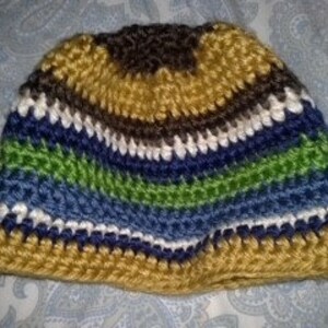 May include: A striped crochet beanie hat in shades of gold, brown, white, blue, and green. The handmade hat is made from thick yarn, suggesting a warm and comfortable accessory for cooler weather.