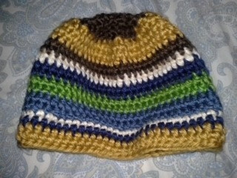 May include: A striped crochet beanie hat in shades of gold, brown, white, blue, and green. The handmade hat is made from thick yarn, suggesting a warm and comfortable accessory for cooler weather.