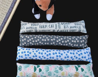 May include: A plush brown and white cat toy positioned above four rectangular fabric cat kicker toys. The top kicker features text including "FARM CAT," the second has white paw prints on gray, the third blue paw prints on white, and the fourth a botanical pattern.
