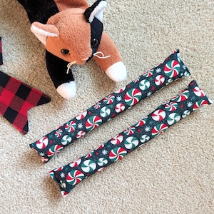 The kicker toys feature a dark green background with a repeating pattern of red and white peppermint candies .Set of 2 holiday catnip cat kickers toys 8X1.5 inches in choice from 6 cotton print fabric.