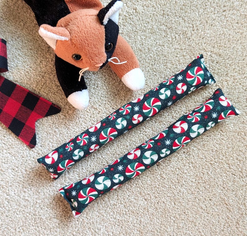 The kicker toys feature a dark green background with a repeating pattern of red and white peppermint candies .Set of 2 holiday catnip cat kickers toys 8X1.5 inches in choice from 6 cotton print fabric.