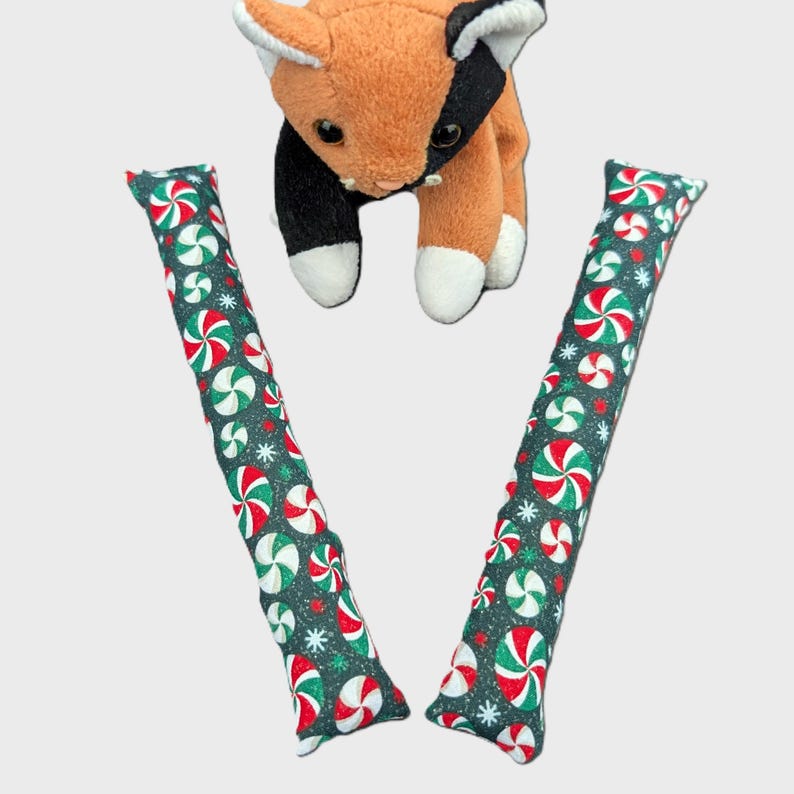 The kicker toys feature a dark green background with a repeating pattern of red and white peppermint candies .Set of 2 holiday catnip cat kickers toys 8X1.5 inches in choice from 6 cotton print fabric.