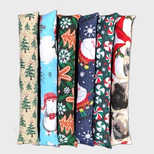 May include: Six long, rectangular fabric tubes featuring various holiday patterns including green Christmas trees, a penguin in a red hat, orange gingerbread shapes, Santa Claus, red and white peppermint candies, and close-up cat faces.