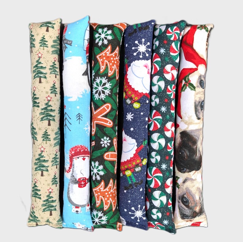 May include: Six long, rectangular fabric tubes featuring various holiday patterns including green Christmas trees, a penguin in a red hat, orange gingerbread shapes, Santa Claus, red and white peppermint candies, and close-up cat faces.